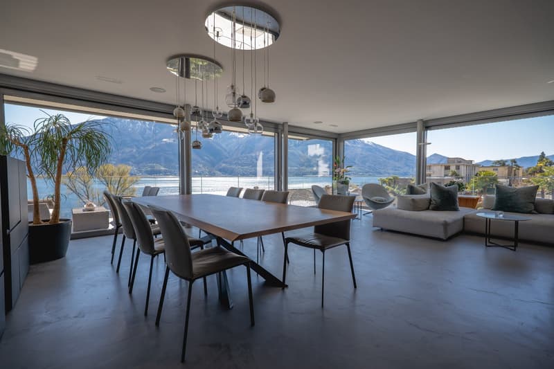 Dining area with large windows, wooden table, modern chairs, large potted plant, modern chandelier, couch, side table, view of mountains and water