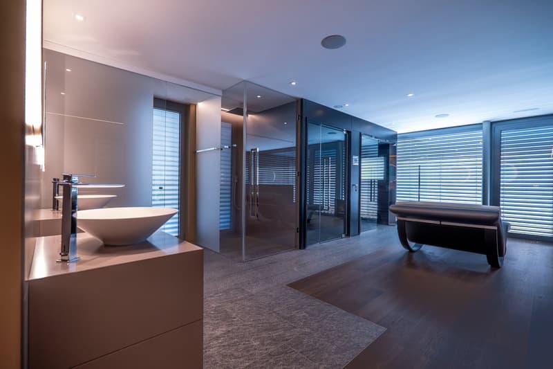 modern bathroom with glass shower, double sink, black leather bench, wooden floor, white walls