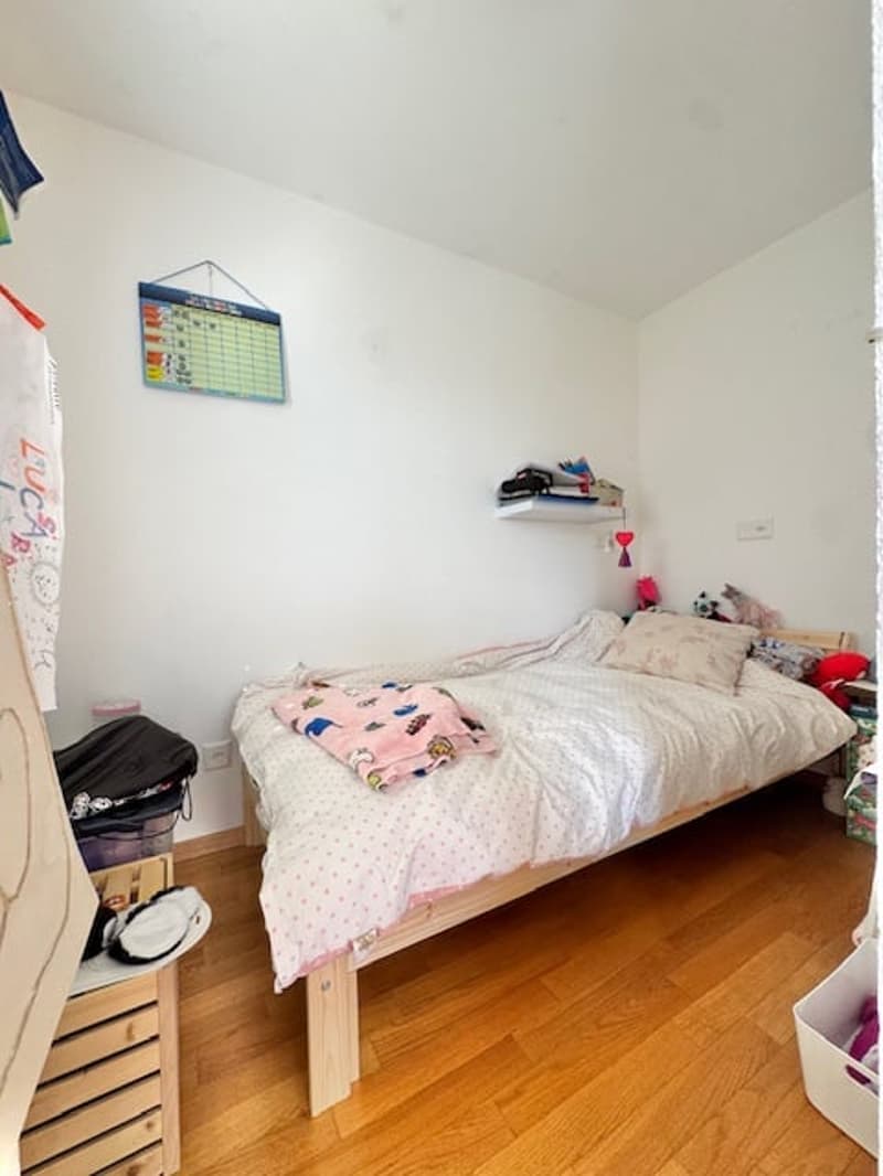 small bedroom with bed, wooden floor, white walls, shelf, storage boxes, toys