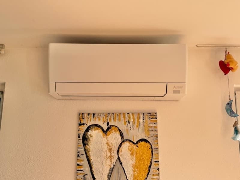 white air conditioner mounted on wall, painting of two hearts, decorative items hanging on wall