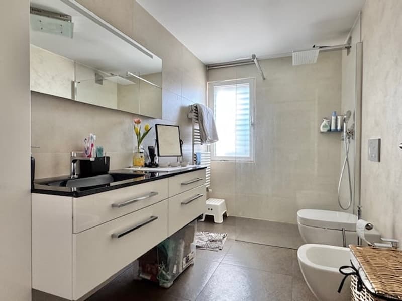 modern bathroom with white tiles, white cabinets, black countertop, white toilet, white bathtub, shower, mirror, and a window