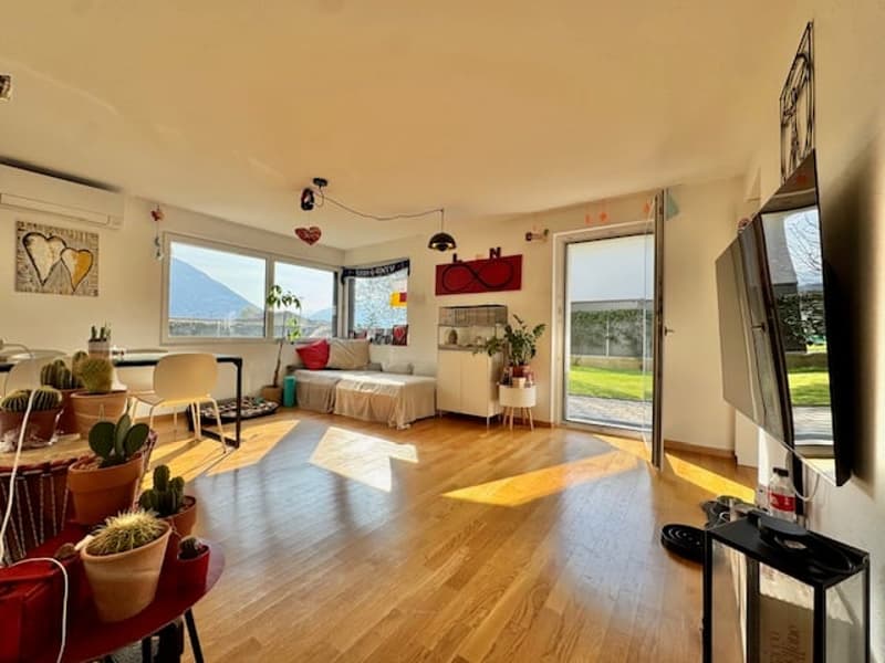 living room with wooden floor, large windows, couch, TV, plants, table, chairs, and a view of the mountains