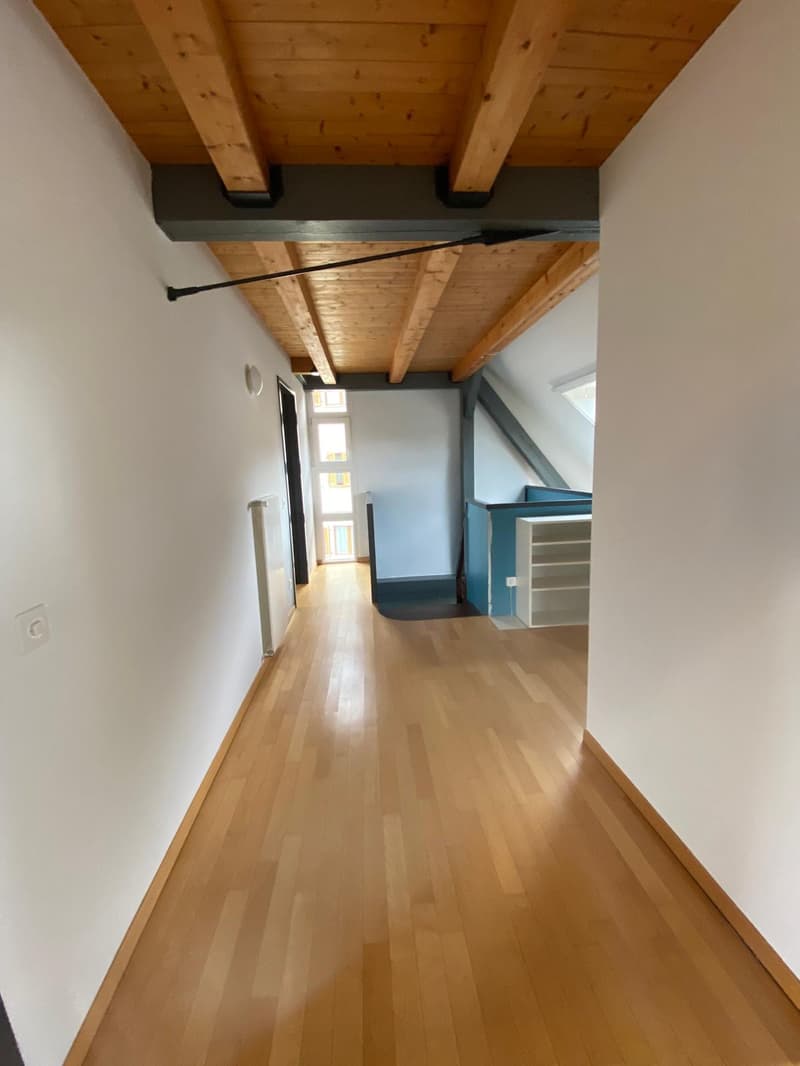 The image shows a hallway with a wooden ceiling and beams, hardwood floors, and white walls. There is a blue cabinet or storage unit visible at the end of the hallway.