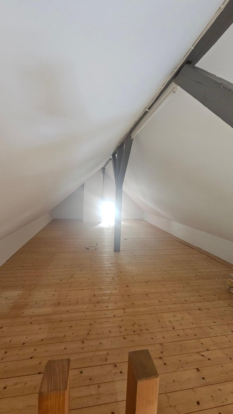 Wooden floor, slanted ceiling, and a light source visible in the corner of the attic space.