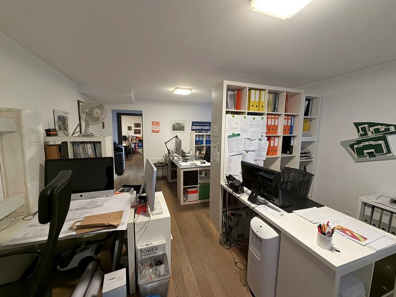 an office with desk, computer monitors, fan, cabinets, and shelves