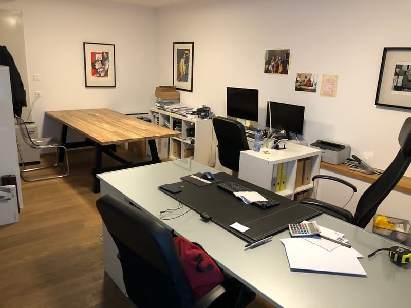 Wooden desk, two chairs, three monitors, printer, white walls, wooden floor.