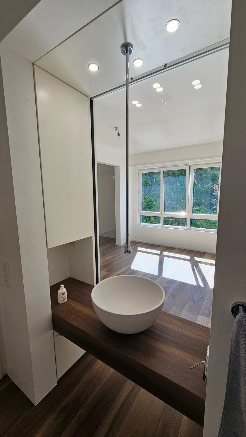 a modern bathroom with a round sink, white tiles, wooden countertop, mirror, shower room, and windows