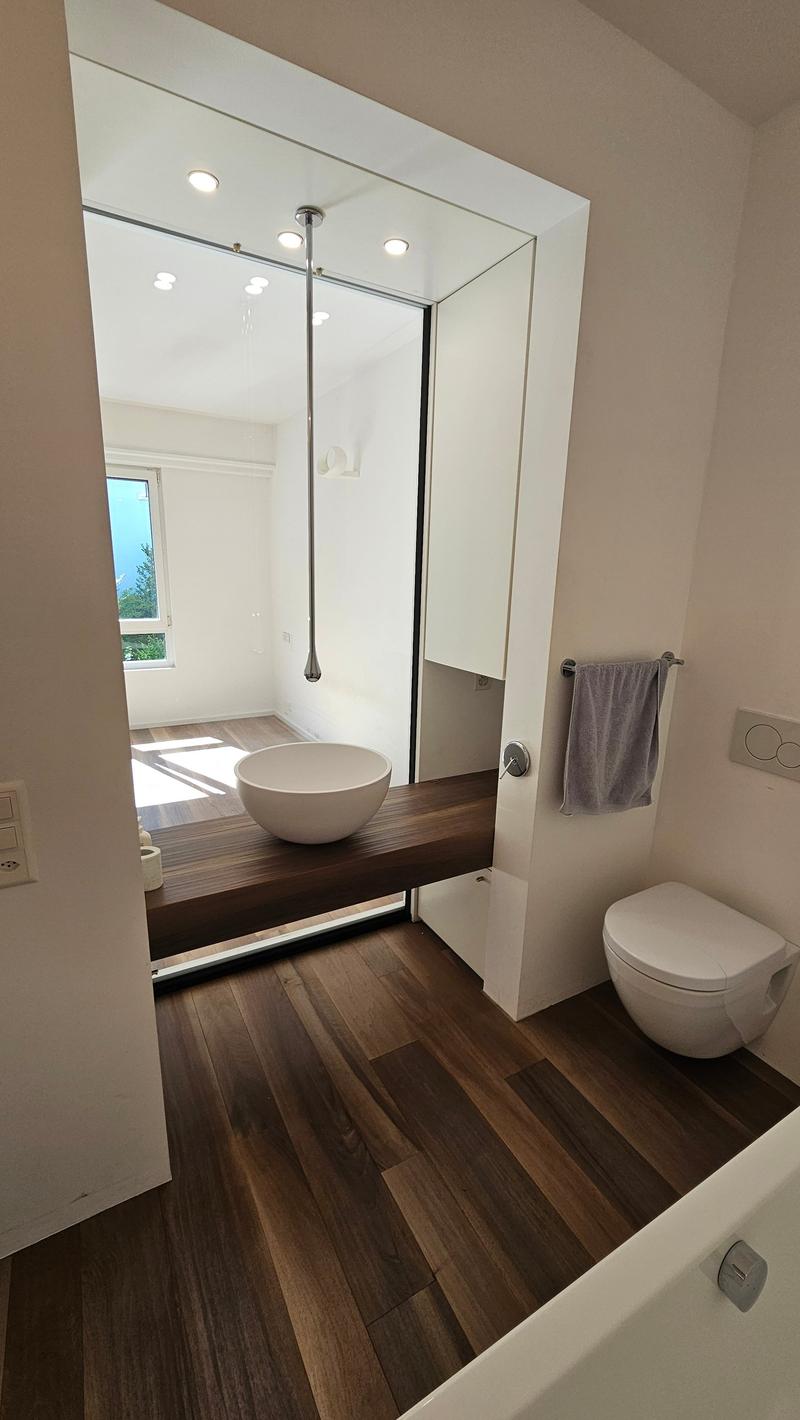 modern design bathroom, large mirror, wooden floor, contemporary fixtures, bathtub, white toilet, white sink, towel rack, window with mountain view