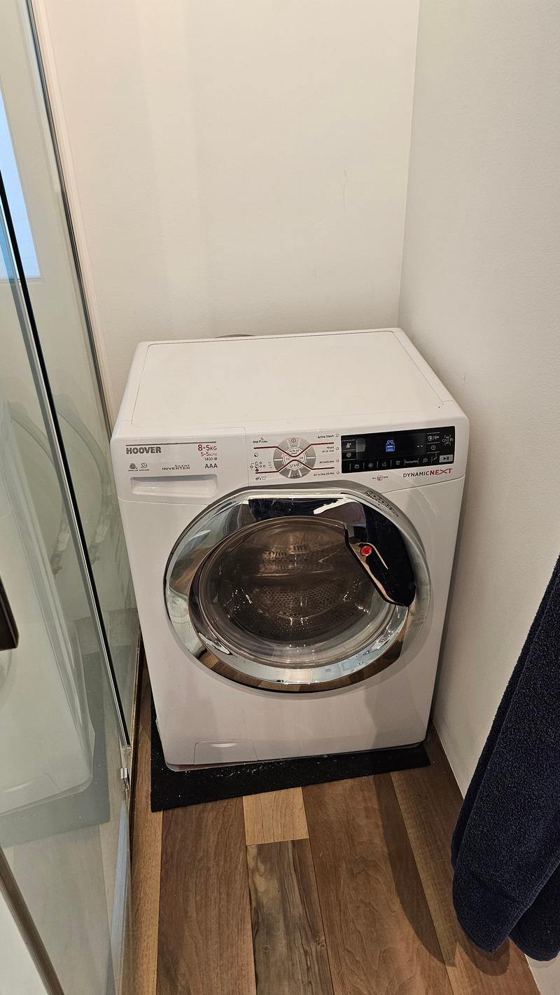 Hoover brand front-load washing machine, black mat on the floor, glass door on the left, towel hanging on the right