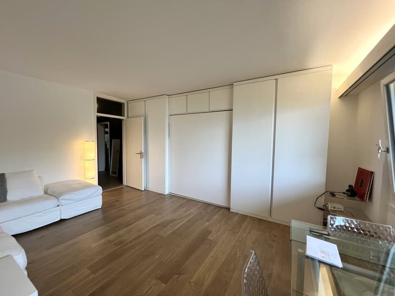 Minimalist interior, white walls, wooden floor, white sectional sofa, white storage cabinets, glass table, white ceiling