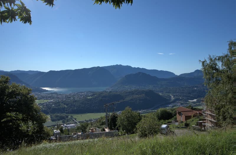 Aerial view of a scenic landscape with mountains, a lake, a town, a crane, and construction sites