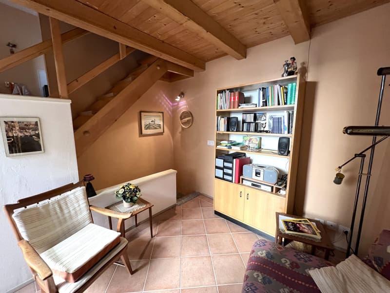 A room with wooden chair, table, bookshelf, couch, and a staircase