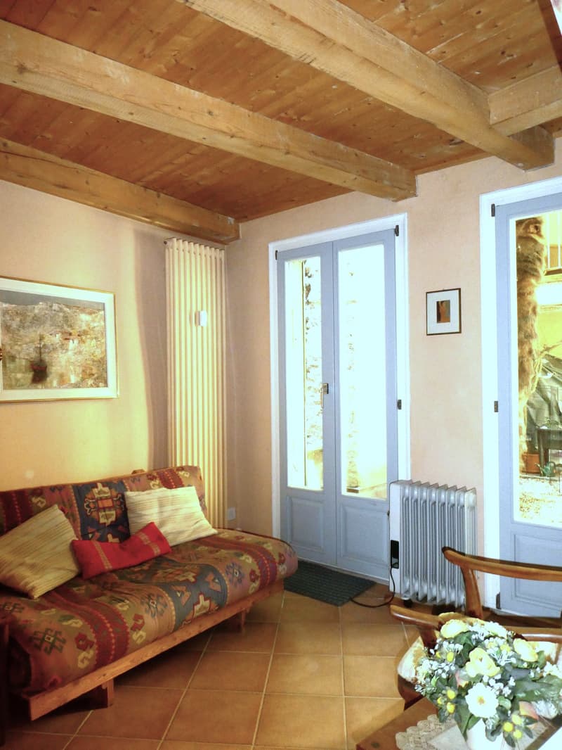 A living room with a couch, wooden beams, tiled floor, radiator, and a picture frame on the wall.