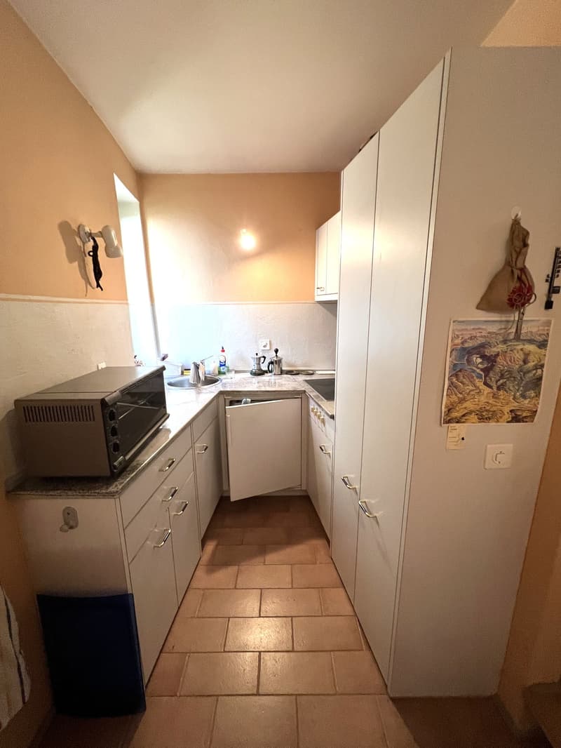 Compact kitchen with white cabinets, tiled floor, sink, microwave, and a small stove.