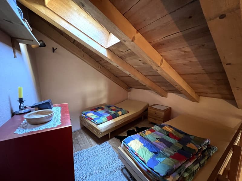 Small bedroom with two beds, wooden ceiling, wooden floor, nightstand, bowl, candle, rug, wooden cabinet