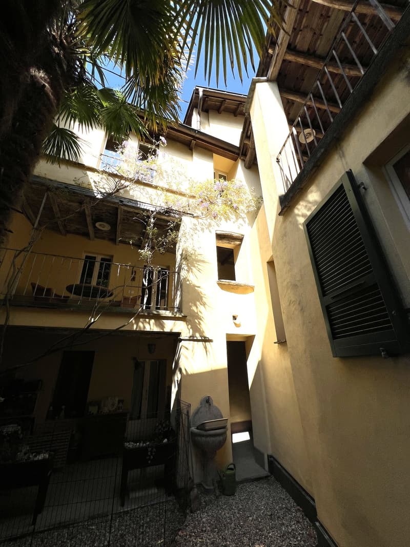 Courtyard with a balcony, yellow walls, gravel floor, a fountain, a table, chairs, and a palm tree