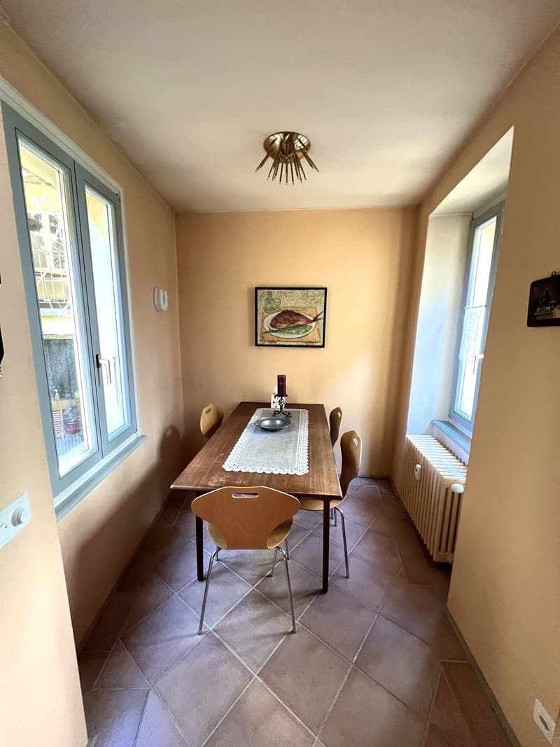 Dining room with wooden table, chairs, tiled floor, windows, radiator, picture frame, candle, plate, and bowl