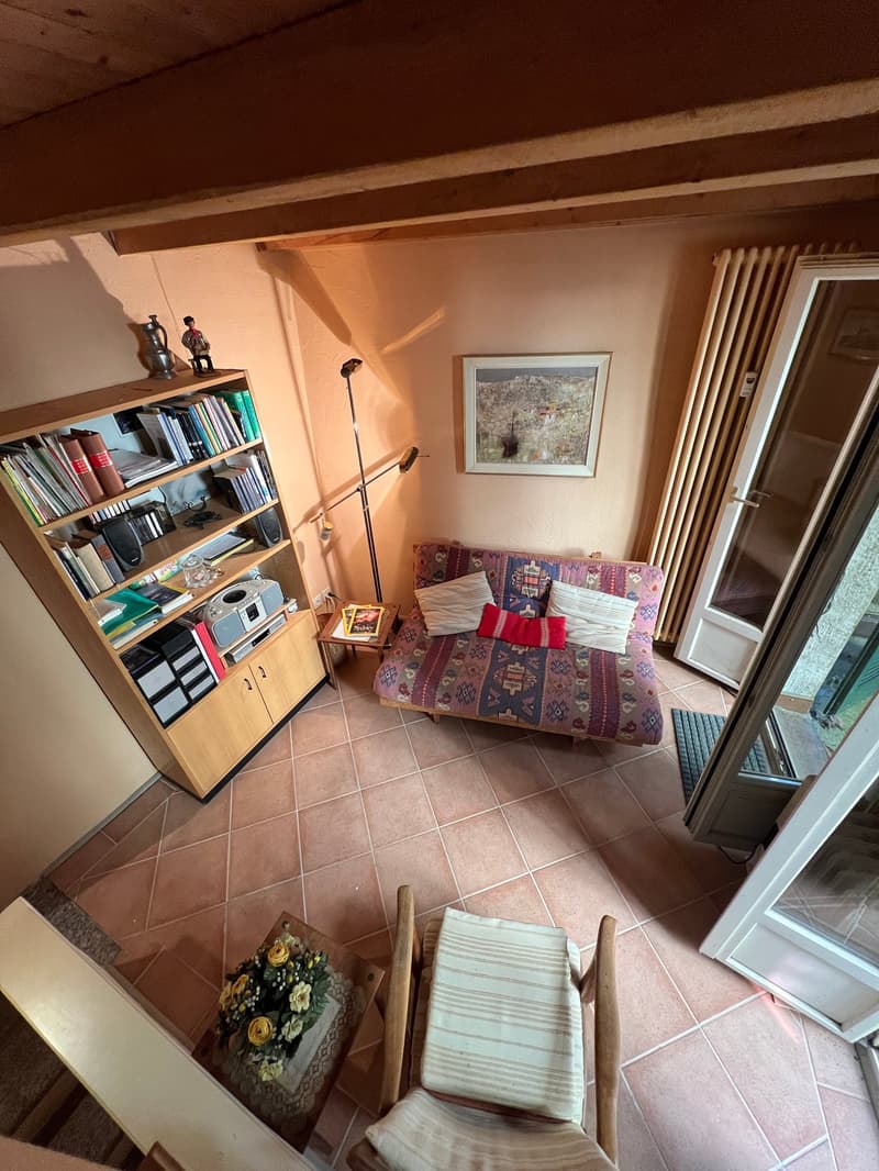 A room with a couch, a bookshelf, a table, a lamp, a picture frame, and a door.