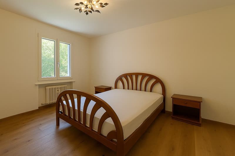 Empty bedroom with wooden bed, two nightstands, white walls, wooden floor, window with white frame, white radiator