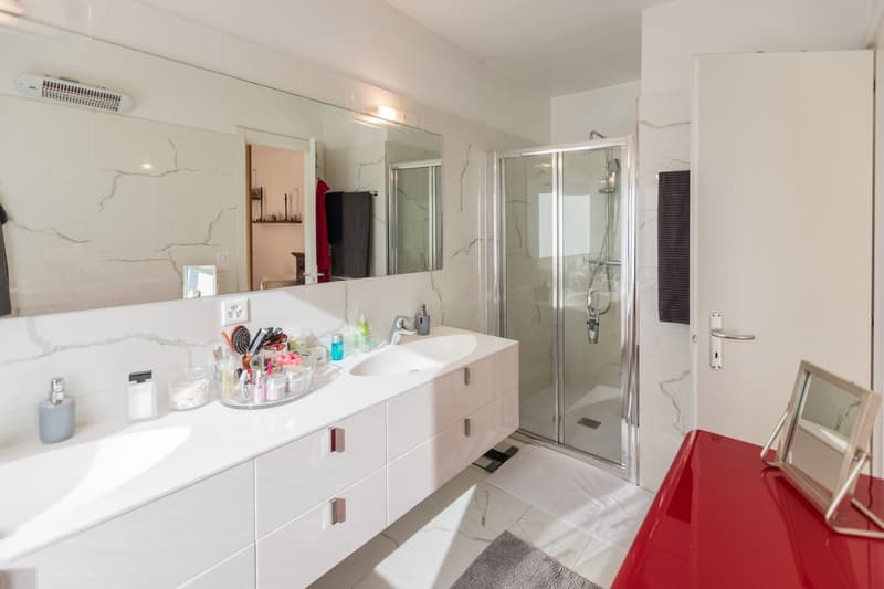 Double sink, large mirror, shower, red table, large white cabinets, towel rack