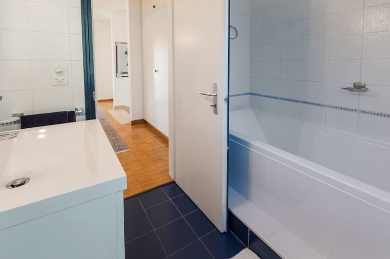 modern bathroom, white walls, blue tiled floor, large bathtub, large sink, towel rack
