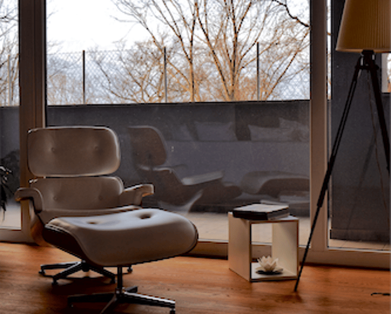 living area with white armchair and ottoman, floor lamp, sliding glass door leading to balcony, view of trees and sky