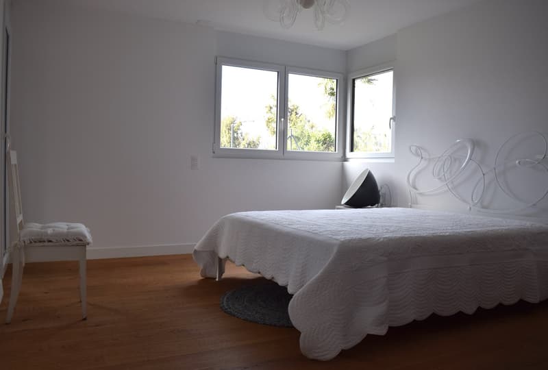 white walls, hardwood floor, queen bed, chair, chandelier, windows with views of the outside