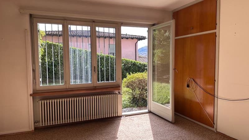 Spacious living room with large windows overlooking a garden, wooden floors, and a radiator along the wall.