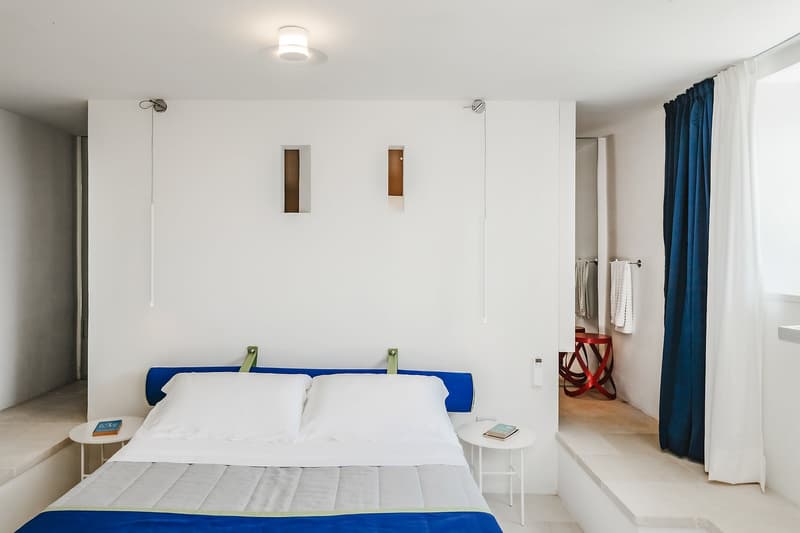 modern bedroom with white walls, blue headboard, white bedding, two nightstands, blue and white curtains