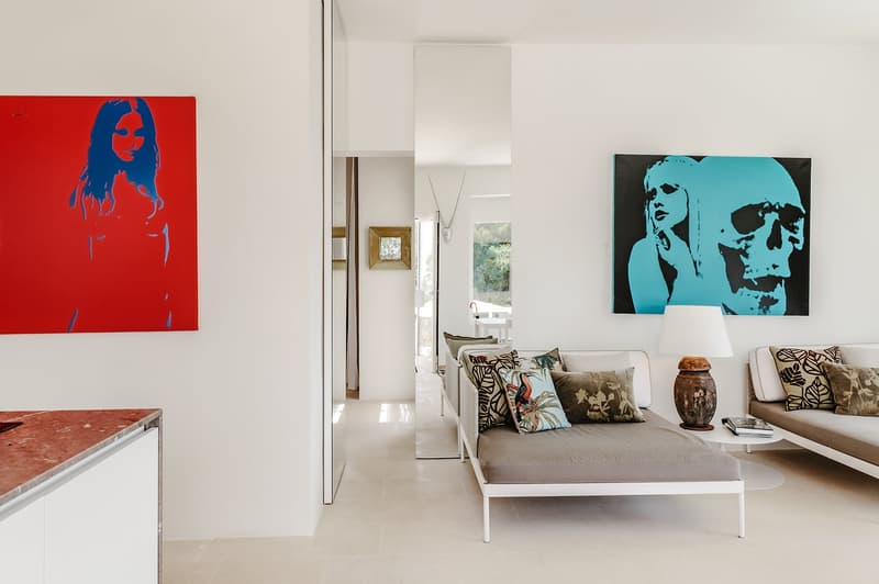 modern living room with white walls, beige floor, two daybeds, lamps, paintings, mirror