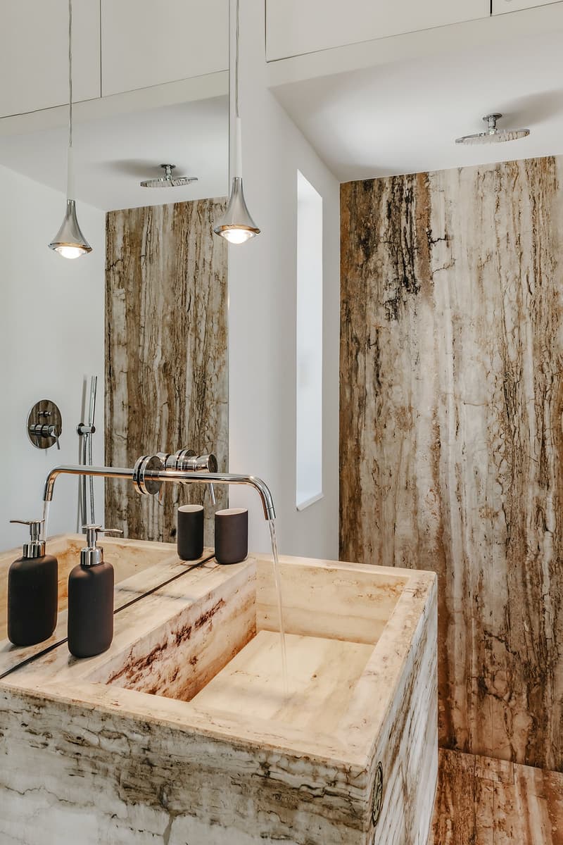 modern bathroom with marble walls, large sink, modern faucet, two soap dispensers, two cups, shower head
