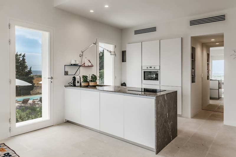 modern kitchen with white cabinets, granite countertop, built-in oven, induction cooktop, large window with view of the sea and garden