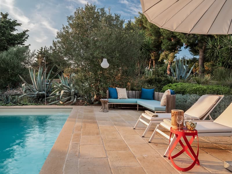 Outdoor area with a swimming pool, lounge chairs, a wooden bench, and a red table with wine glasses