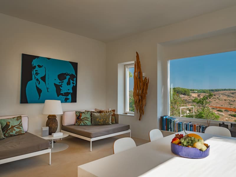 modern room with white walls, two beds, a sofa, a table, a lamp, a painting, and a window with a view