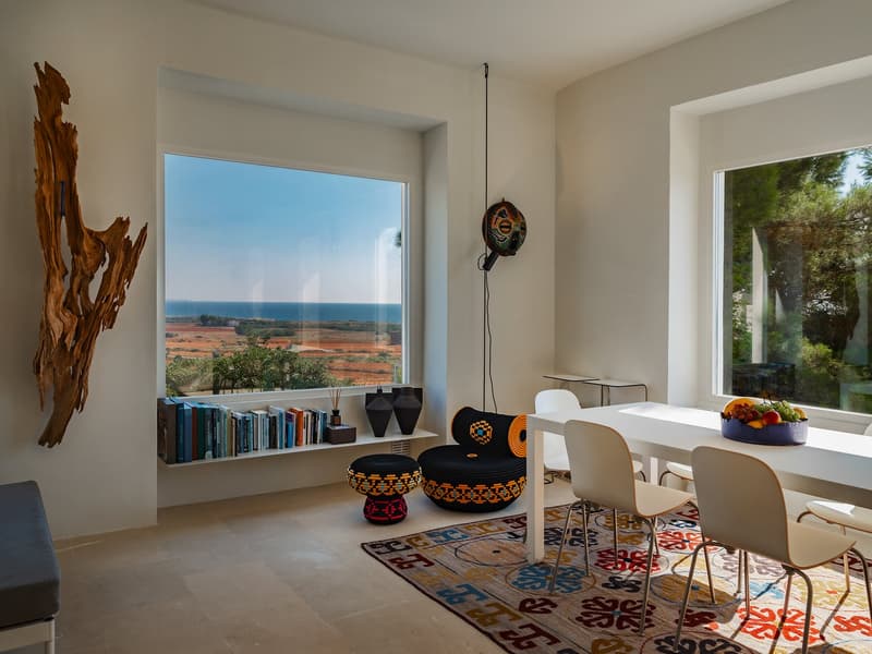 Dining room with large windows, white walls, white table and chairs, decorative rug, and a view of the ocean