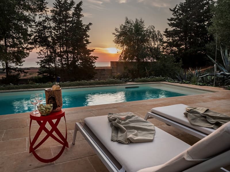 Outdoor area with a swimming pool, lounge chairs, a table, and a view of the sunset