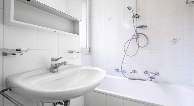 Bathroom with white tiles, white bathtub, white sink, shower head and faucet