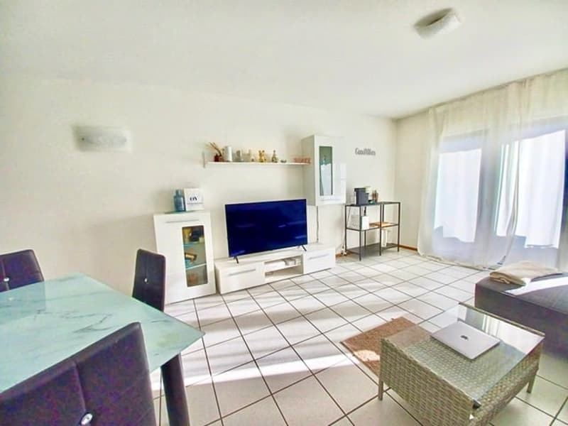 living room with white tiles, large windows, flat screen TV, coffee table, dining table, gray chairs, couch