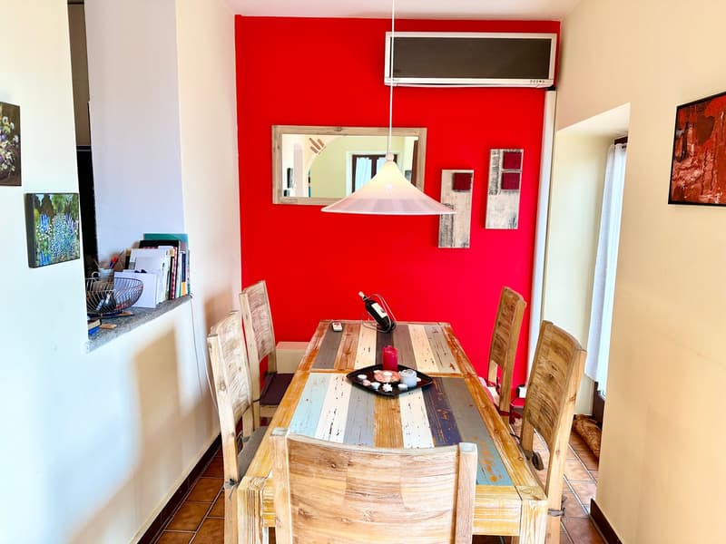 Dining room with wooden table and chairs, red wall, mirror, and artwork