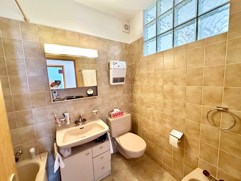 Bathroom with bathtub, sink, toilet, mirror, and tiled walls