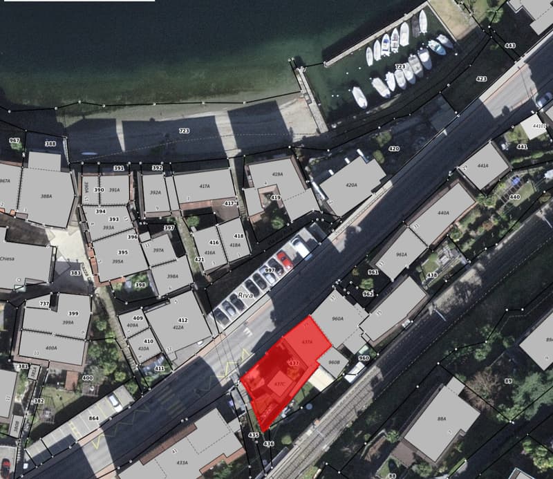Aerial view of a residential area with multiple buildings, roads, and parking lots. The buildings are numbered and have different sizes and shapes. The area is surrounded by trees and plants.