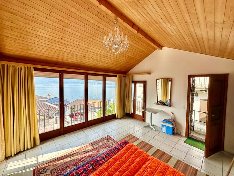 large room with wooden ceiling, chandelier, large windows, balcony, tiled floor, rug, orange bedspread, table, mirror, curtains
