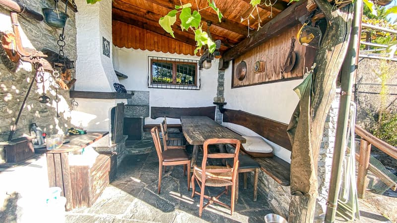 outdoor dining space with fireplace, wooden dining table, wooden chairs, stone walls, wooden beams