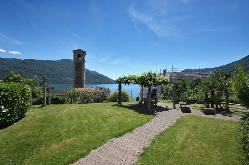 lawn, pergola, bench, plants, building in the background, mountains, water, sky