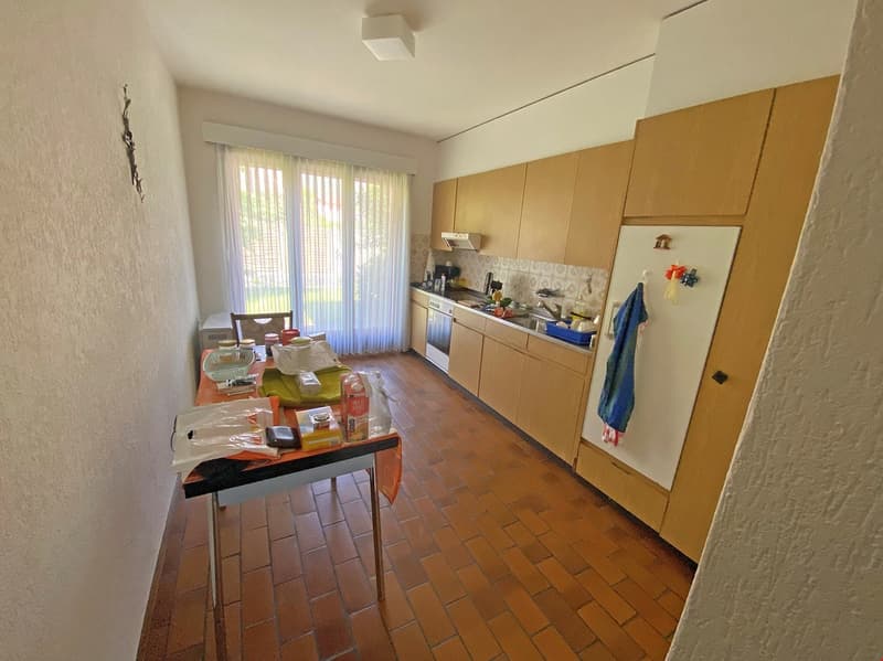 Spacious kitchen with wooden cabinets, tiled floor, large windows, and a washing machine visible.
