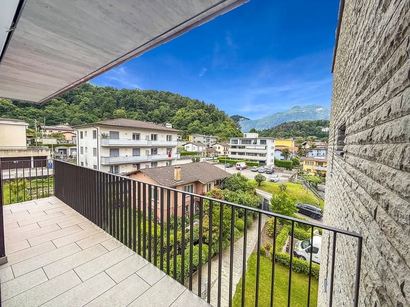 Balcony with a view of a residential neighborhood, surrounded by trees and mountains in the background. The buildings appear to be multi-story apartment complexes.