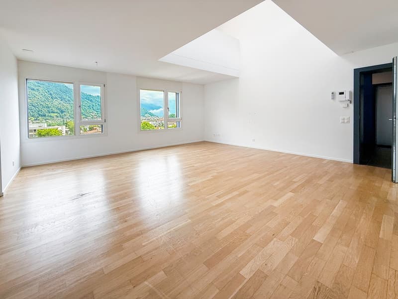Spacious living room with large windows offering a scenic view of the surrounding mountains, hardwood flooring, and a bright, open layout