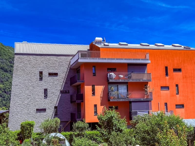 Multi-story apartment building with orange and gray exterior, balconies, and surrounded by greenery