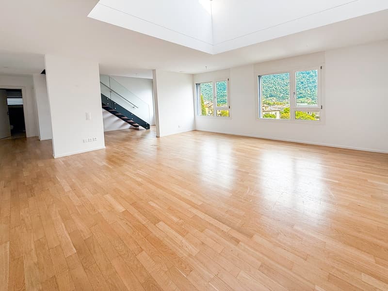 Spacious open-plan living room with hardwood flooring, large windows providing a scenic view, and a staircase leading to another level
