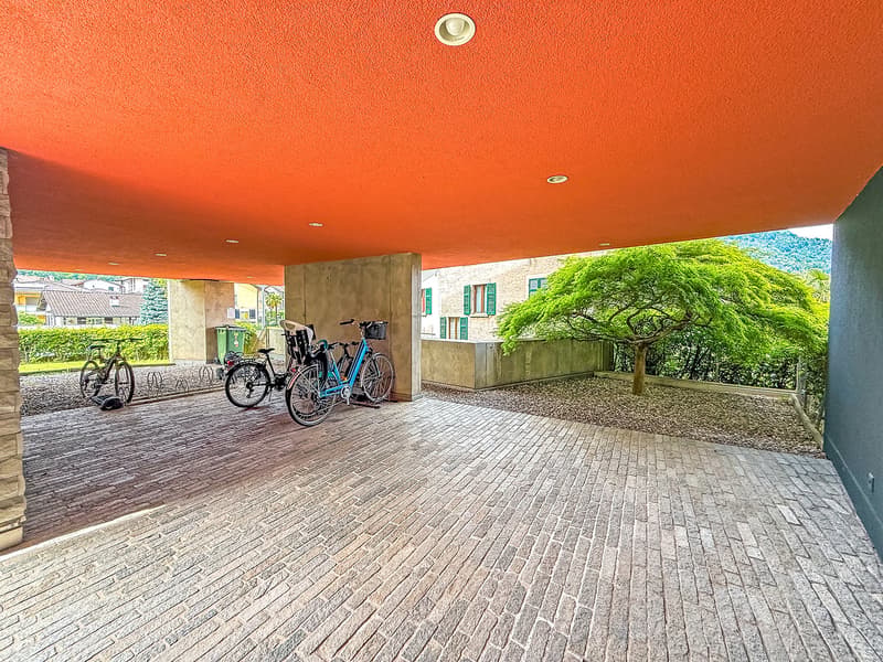 Covered outdoor area with brick flooring, bicycle parking, and a large tree providing shade
